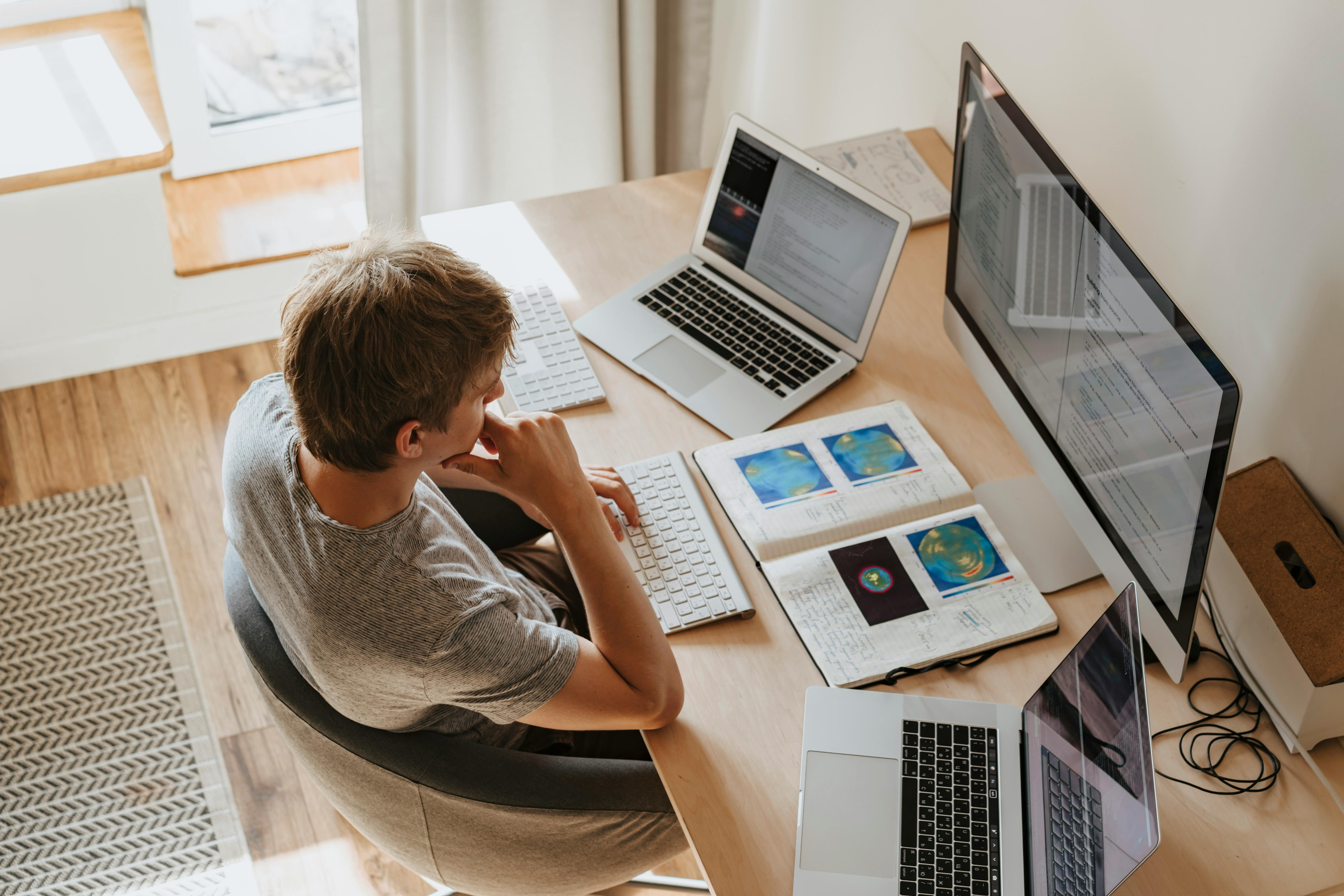 Student studying at desk with multiple computer monitors and books, demonstrating modern digital learning environment
